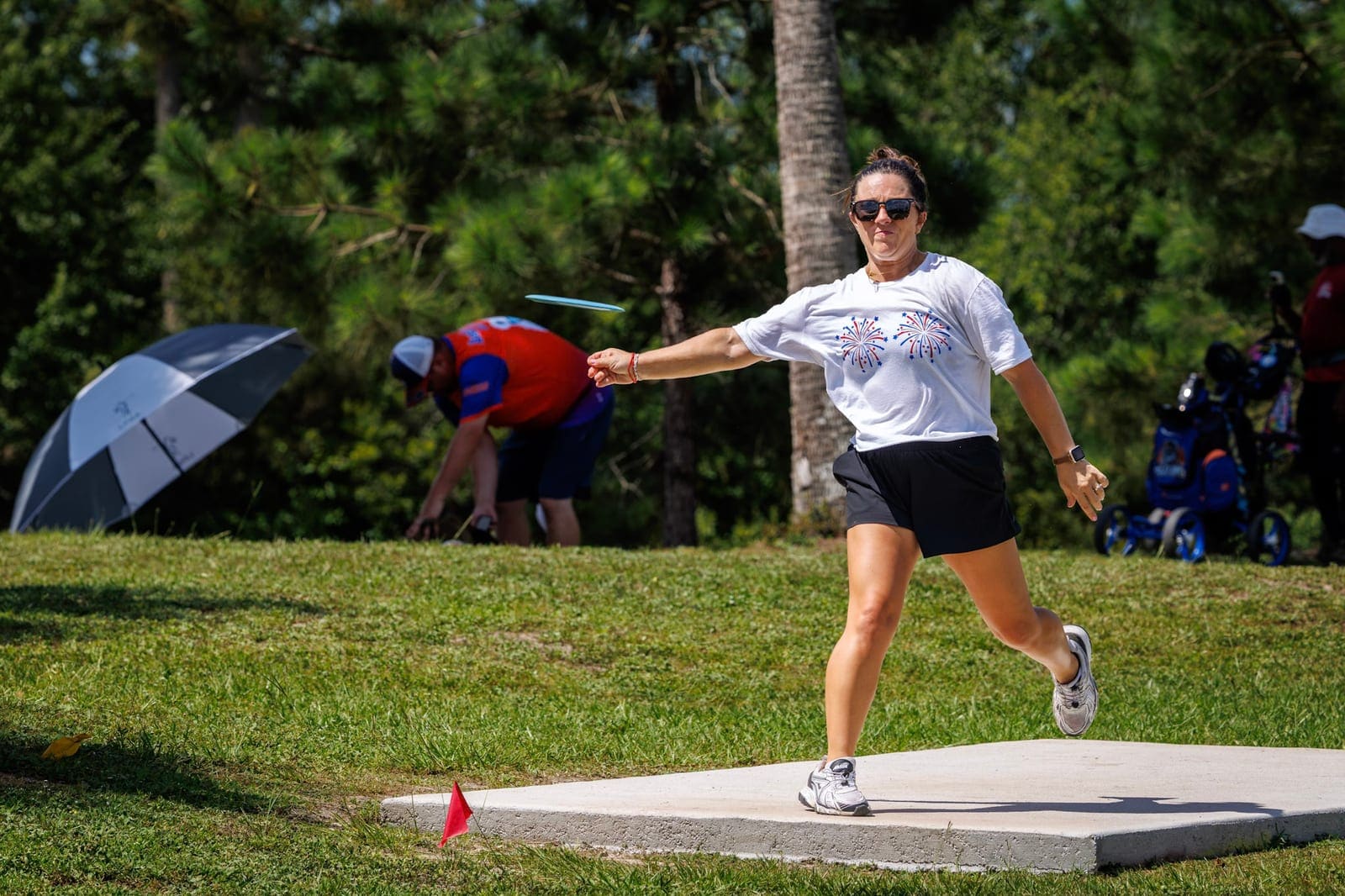 A player runs up to the tee pad and releases a drive, palms and bright sky behind.
