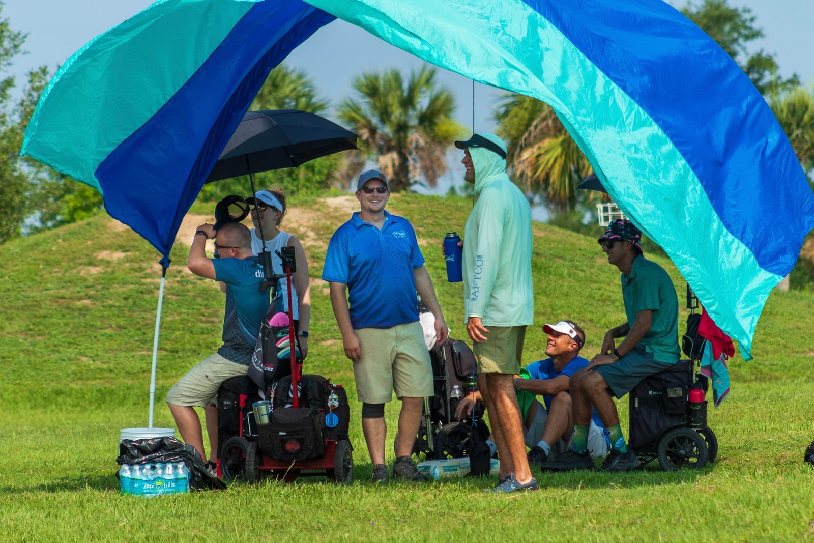 Three players in wheelchairs and their cards wait out the July heat under a shade canopy.