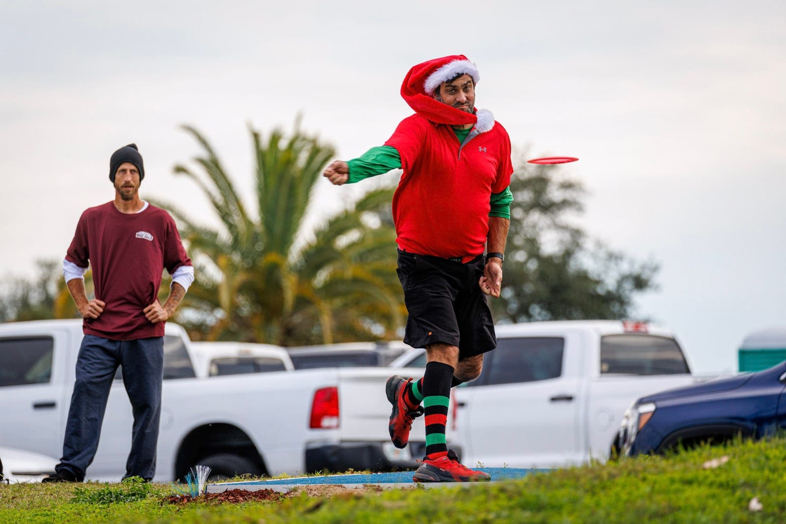 A player in a Christmas sweater, Santa hat and striped socks throws from the tee.